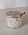 Speckled ceramic container with a wooden handle on a neutral background