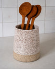 Speckled ceramic utensil holder with wooden spoons against a tiled wall background
