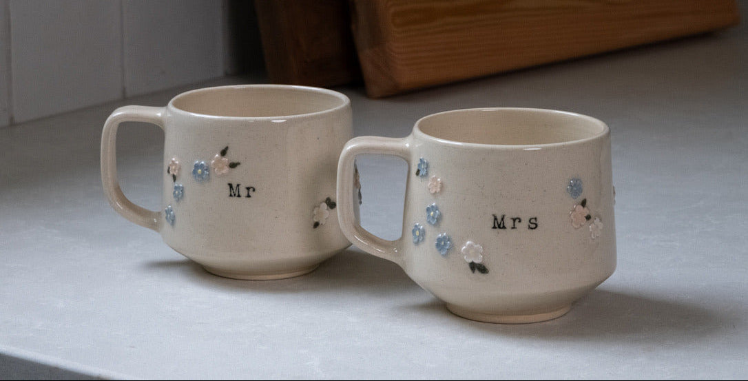 Two ceramic mugs labeled 'Mr' and 'Mrs' on a light surface.