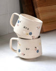 Two stacked ceramic mugs with 'Mrs.' and 'Mr.' text on a white surface.