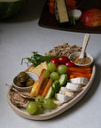 Platter of assorted snacks including olives, grapes, and cheese on a ceramic charcuterie board.
