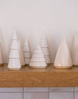 Row of white ceramic Christmas trees on a wooden shelf against a light-colored wall.