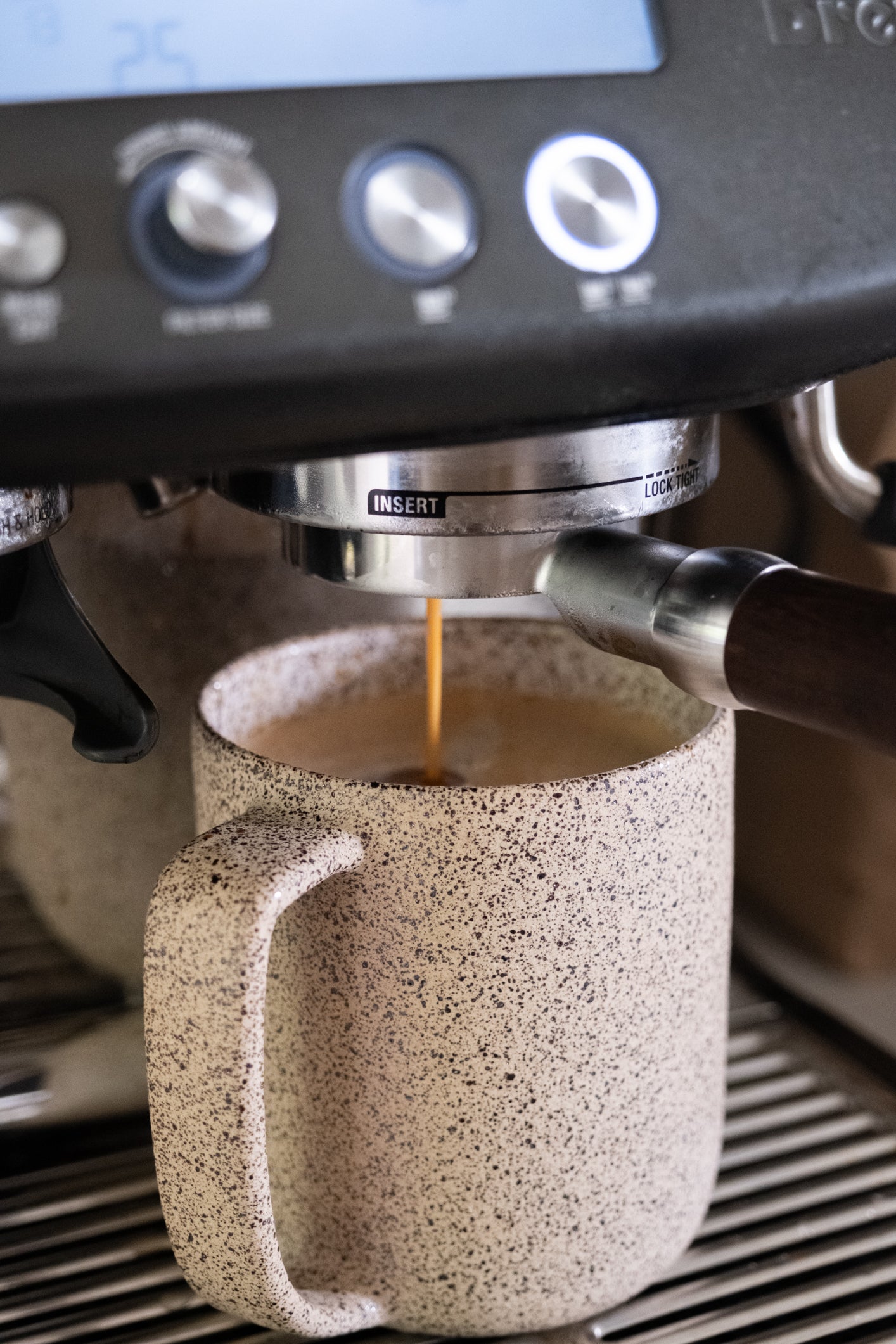 Espresso being poured into a speckled ceramic mug from a coffee machine.