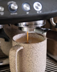 Espresso being poured into a speckled ceramic mug from a coffee machine.