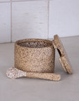 Speckled ceramic jar with lid and scrub brush on a light surface with tiled wall background