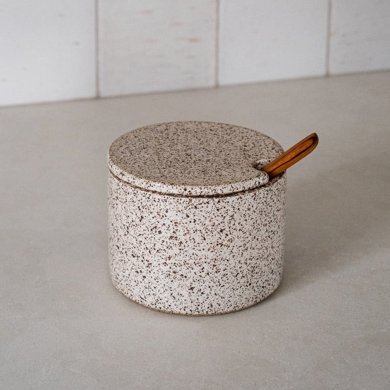 Speckled ceramic container with a wooden handle on a neutral background