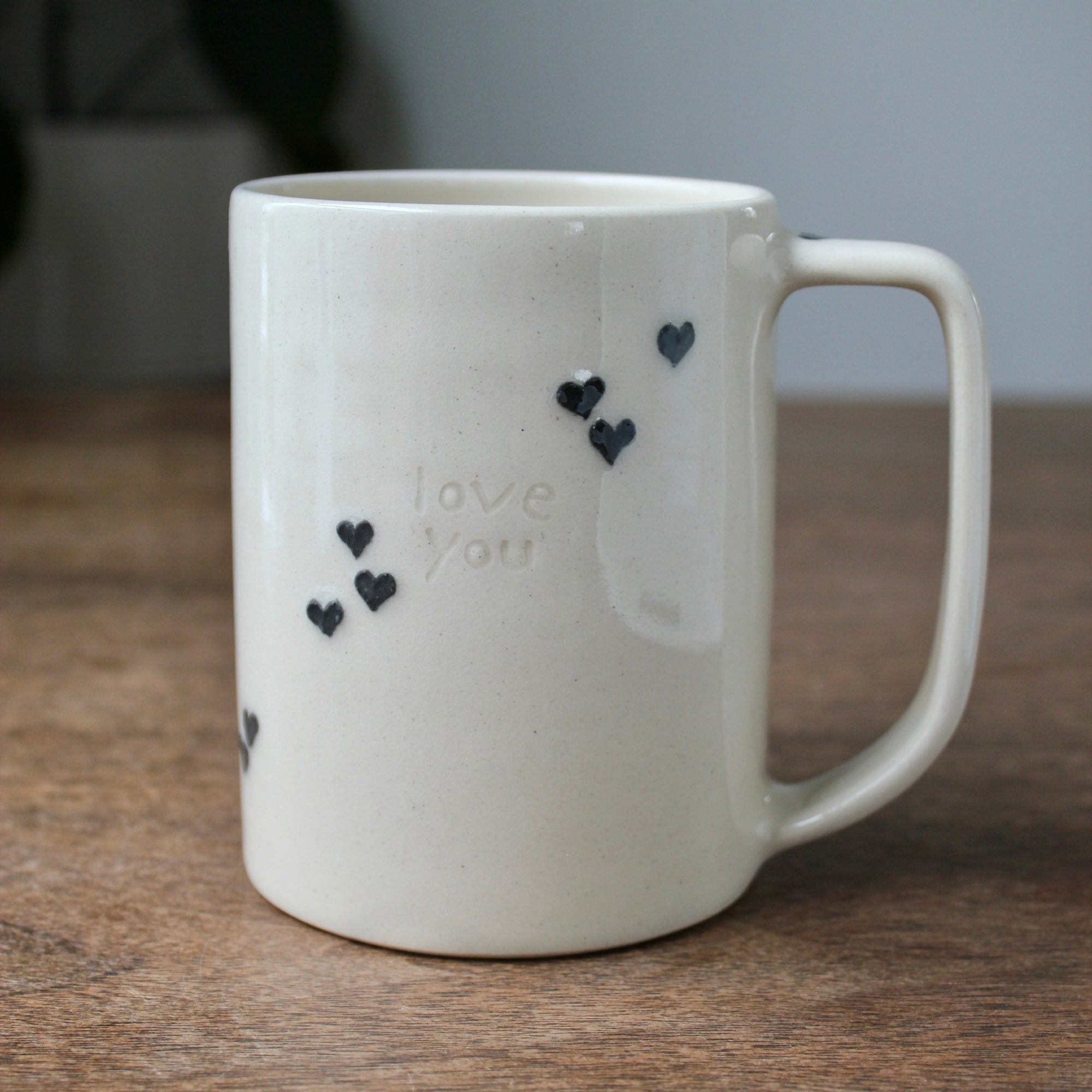 White mug with black heart designs and 'love you' text on a wooden surface
