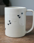 White mug with black heart designs and 'love you' text on a wooden surface