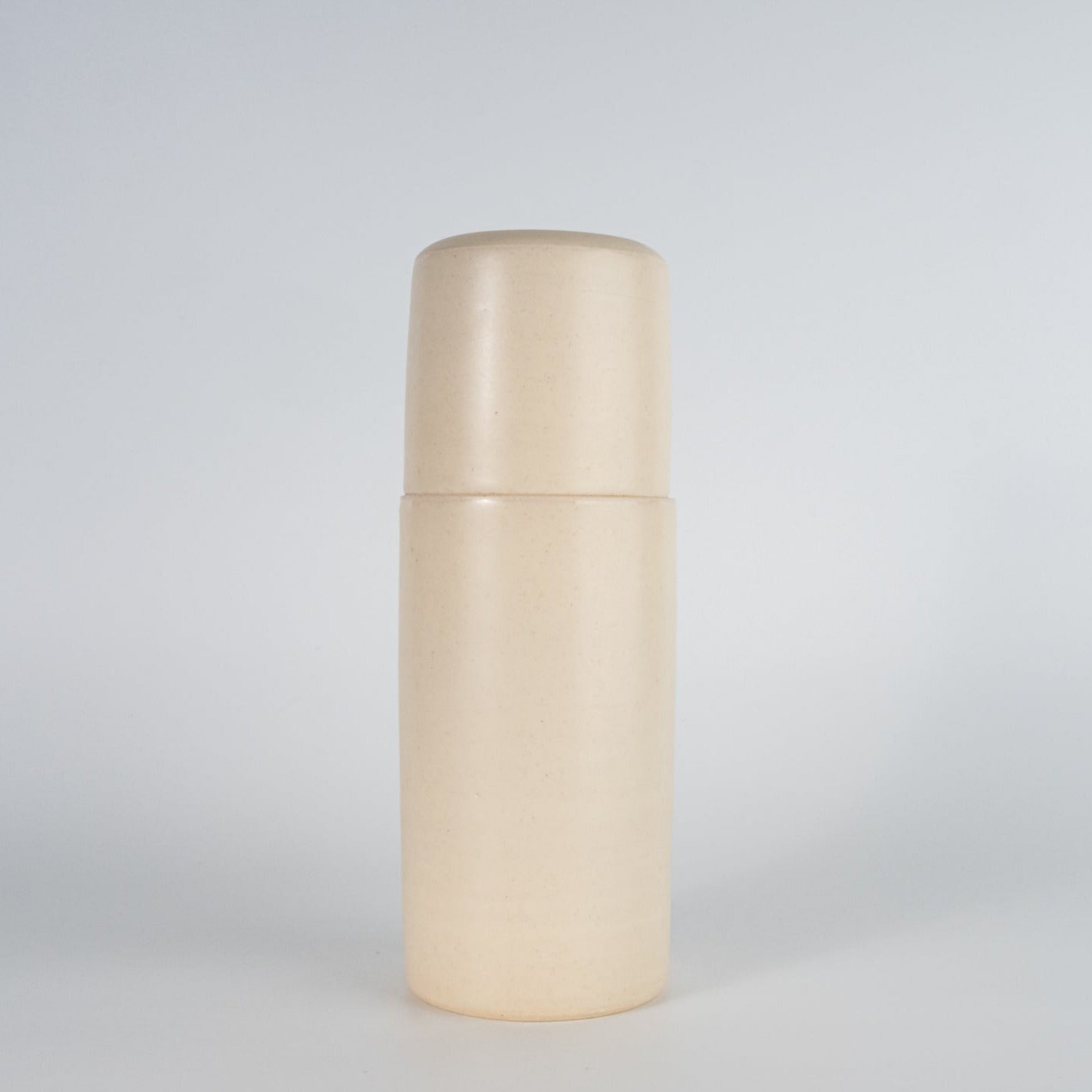 A beige ceramic carafe and tumbler set on a plain background.