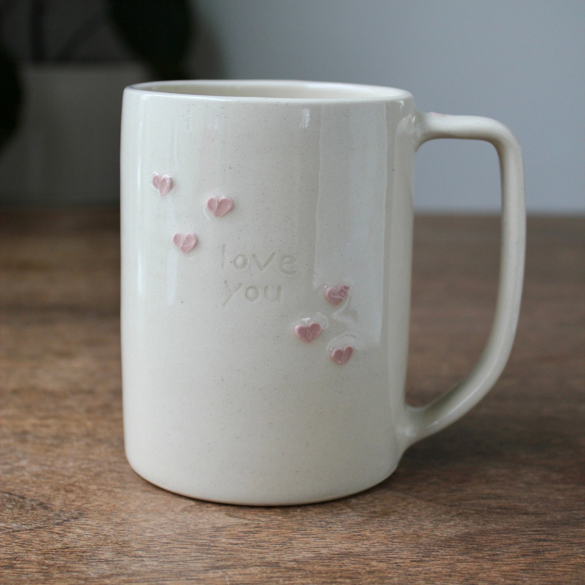 White mug with pink heart designs and 'love you' text on a wooden surface