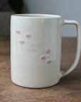White mug with pink heart designs and 'love you' text on a wooden surface