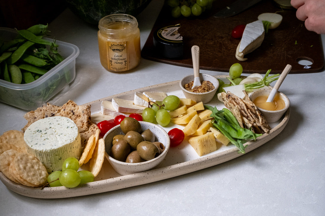 Platter of assorted cheeses, crackers, and fruits with a jar of mustard on a table.