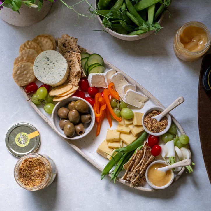 Platter of assorted cheeses, crackers, and vegetables on a white surface with a cutting board and additional food items.