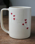 White mug with red heart designs and 'love you' text on a wooden surface