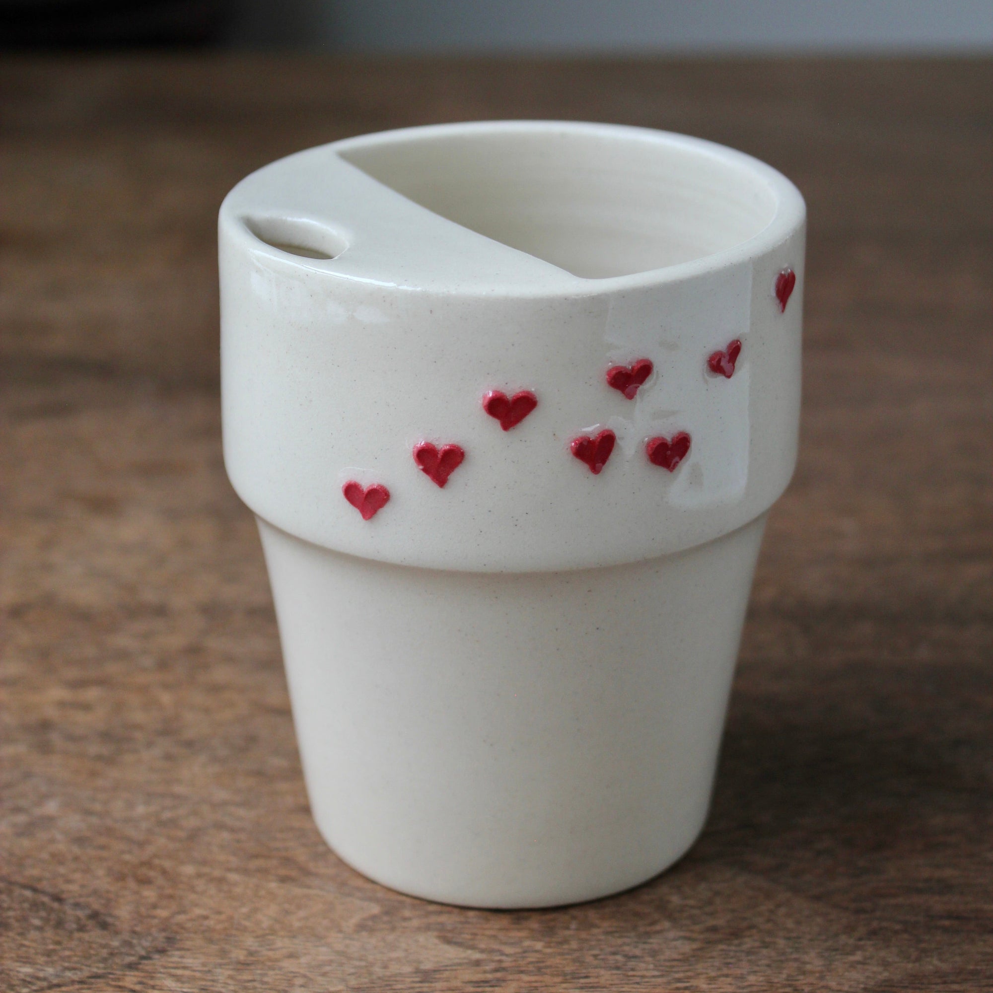 White ceramic cup with red heart designs on a wooden surface