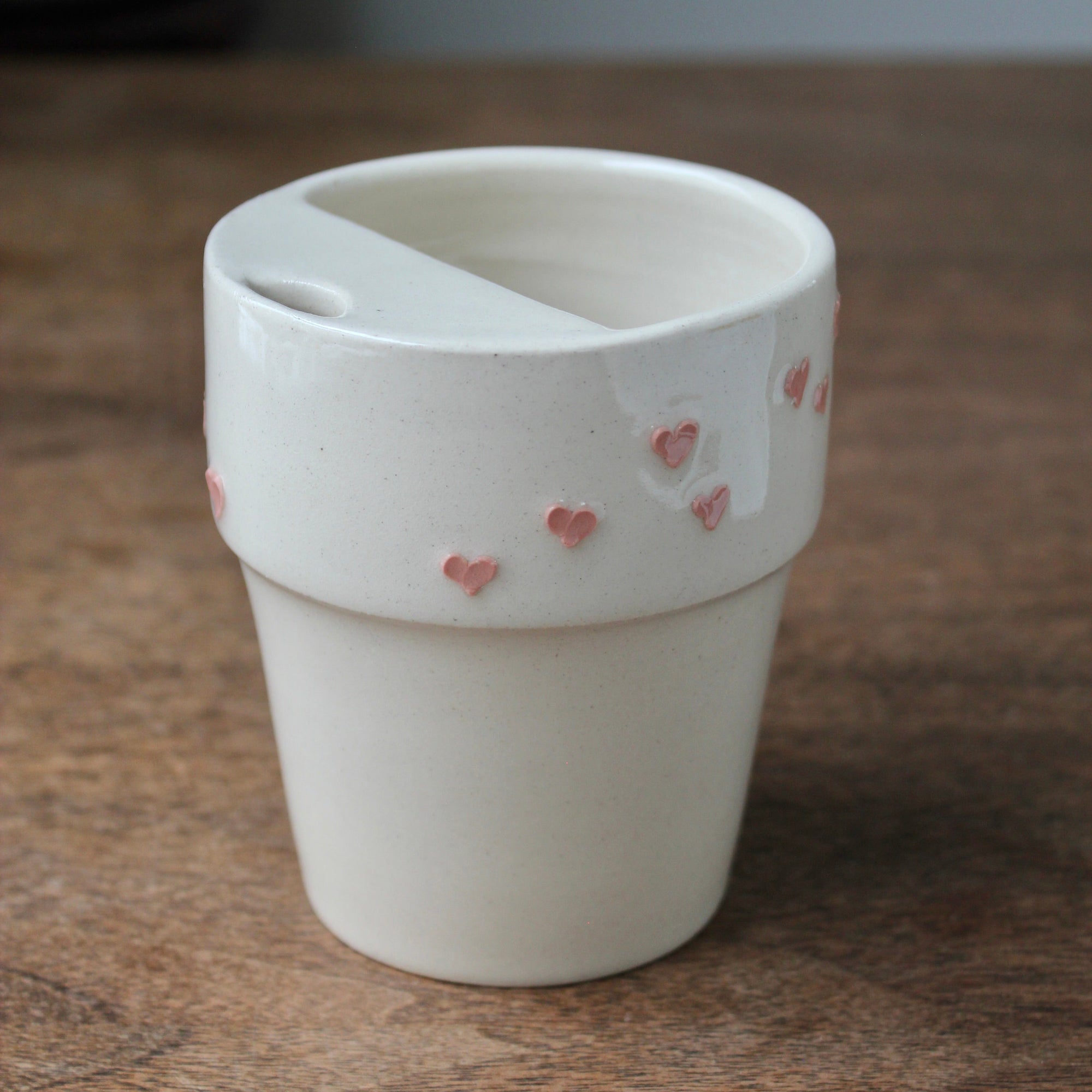 White ceramic cup with pink heart designs on a wooden surface