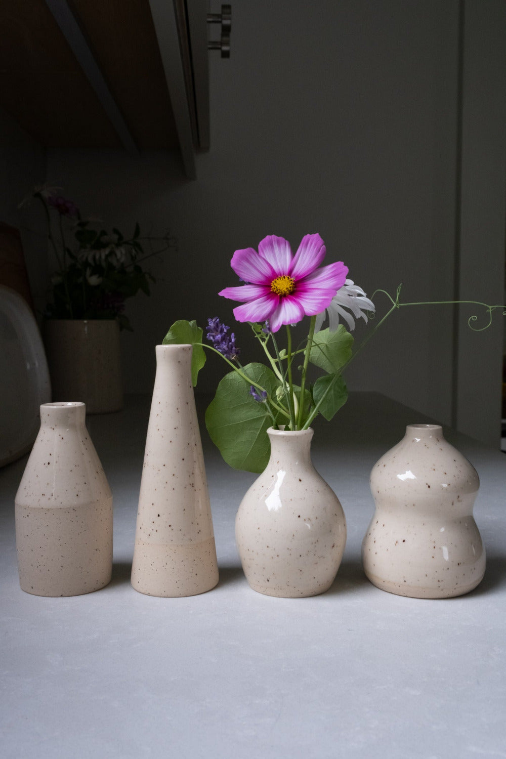 Set of four ceramic vases on a gray surface with a pink flower arrangement.