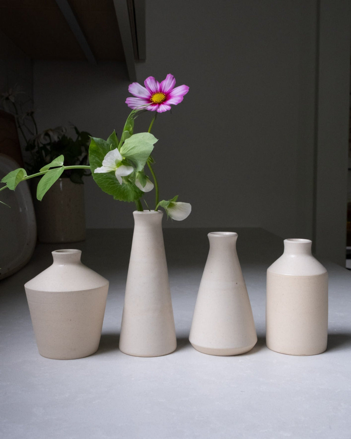 Set of four ceramic vases on a gray surface with a single flower.