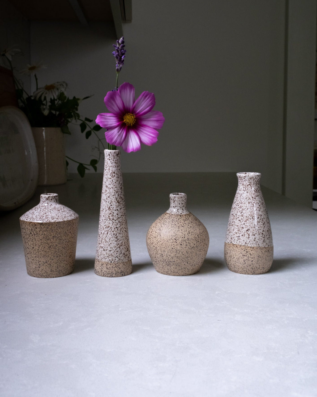 Set of four textured vases with a single pink flower on a light surface.