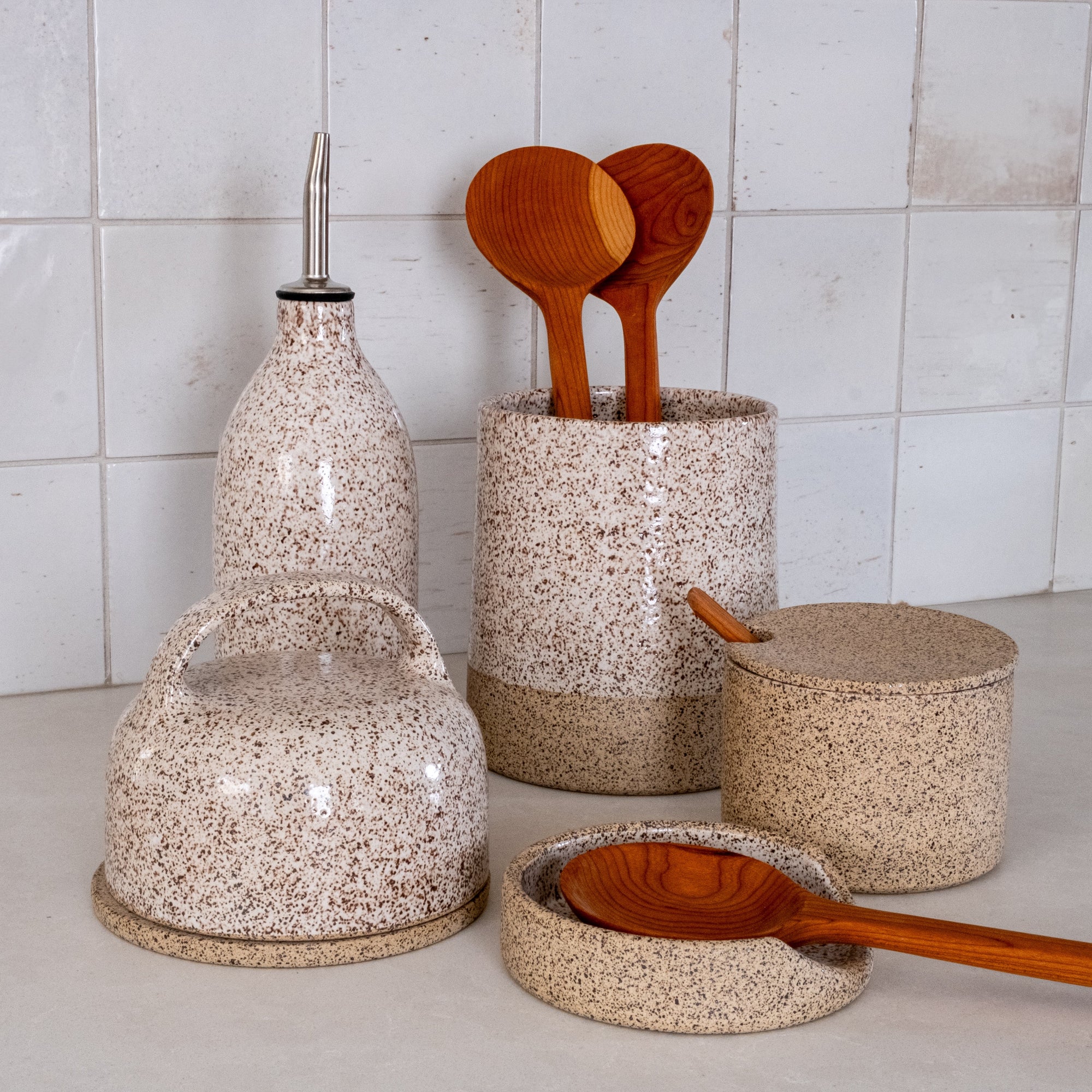 Speckled kitchen ceramic containers with wooden spoons on a tiled wall background